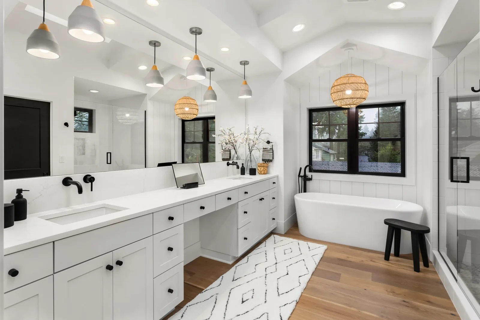 Bathroom with a white double vanity, a freestanding tub, black fixtures and wood flooring