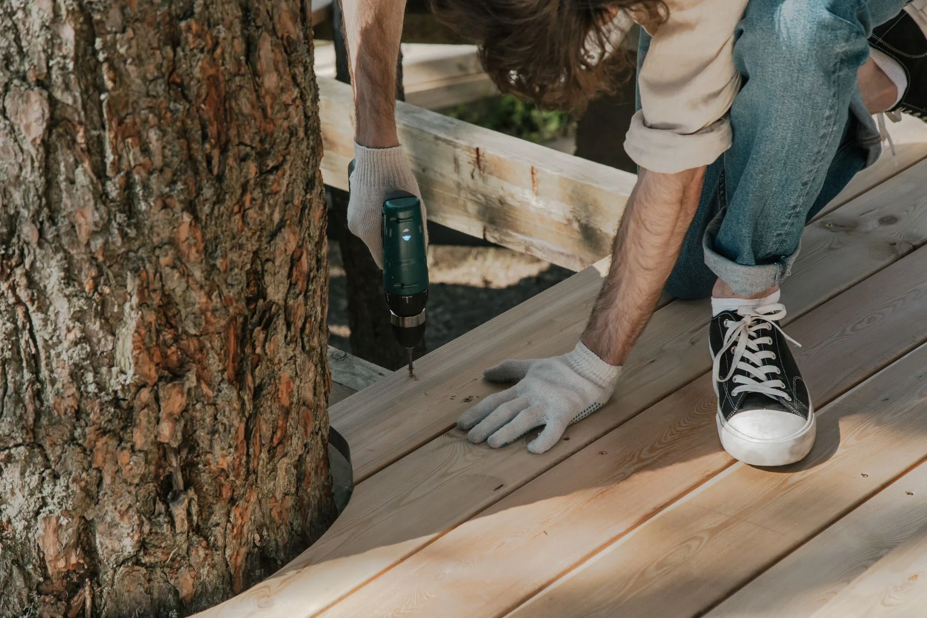 Carpenter fastening fitted deck boards around a mature tree trunk
