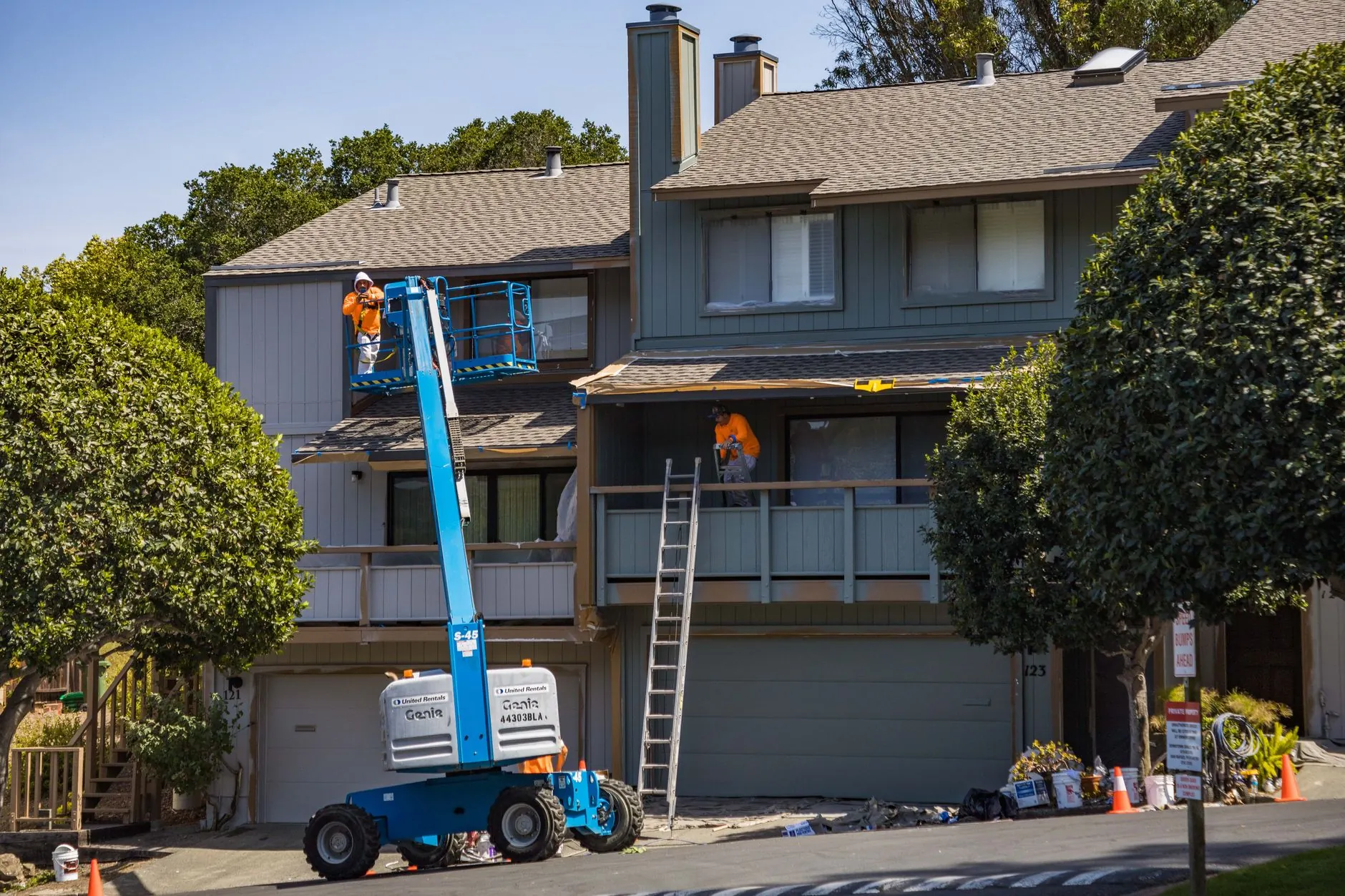 Painters working from a lift and ladders on the exterior of a two-story house