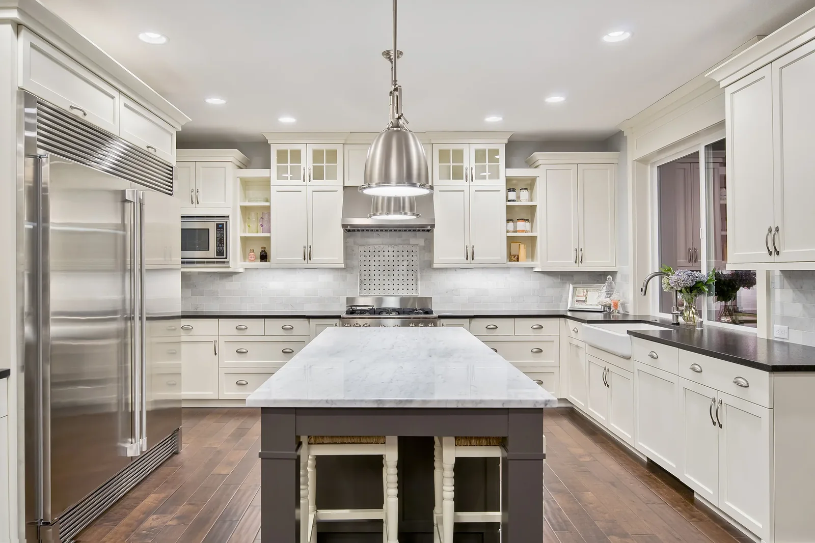 Traditional white kitchen with a marble topped island, wood bar stools and a pendant light