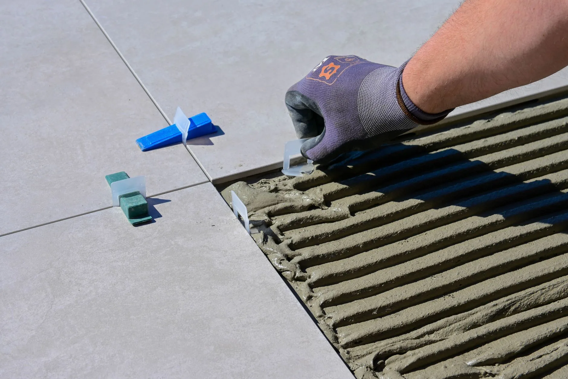 Gloved hand setting a large gray floor tile into combed mortar